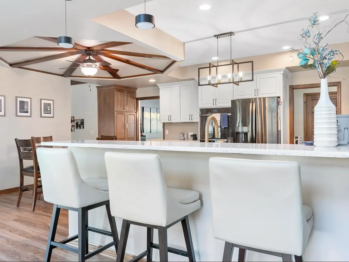 Open-concept kitchen and dining area with white bar stools, wood accents, and a ceiling fan.