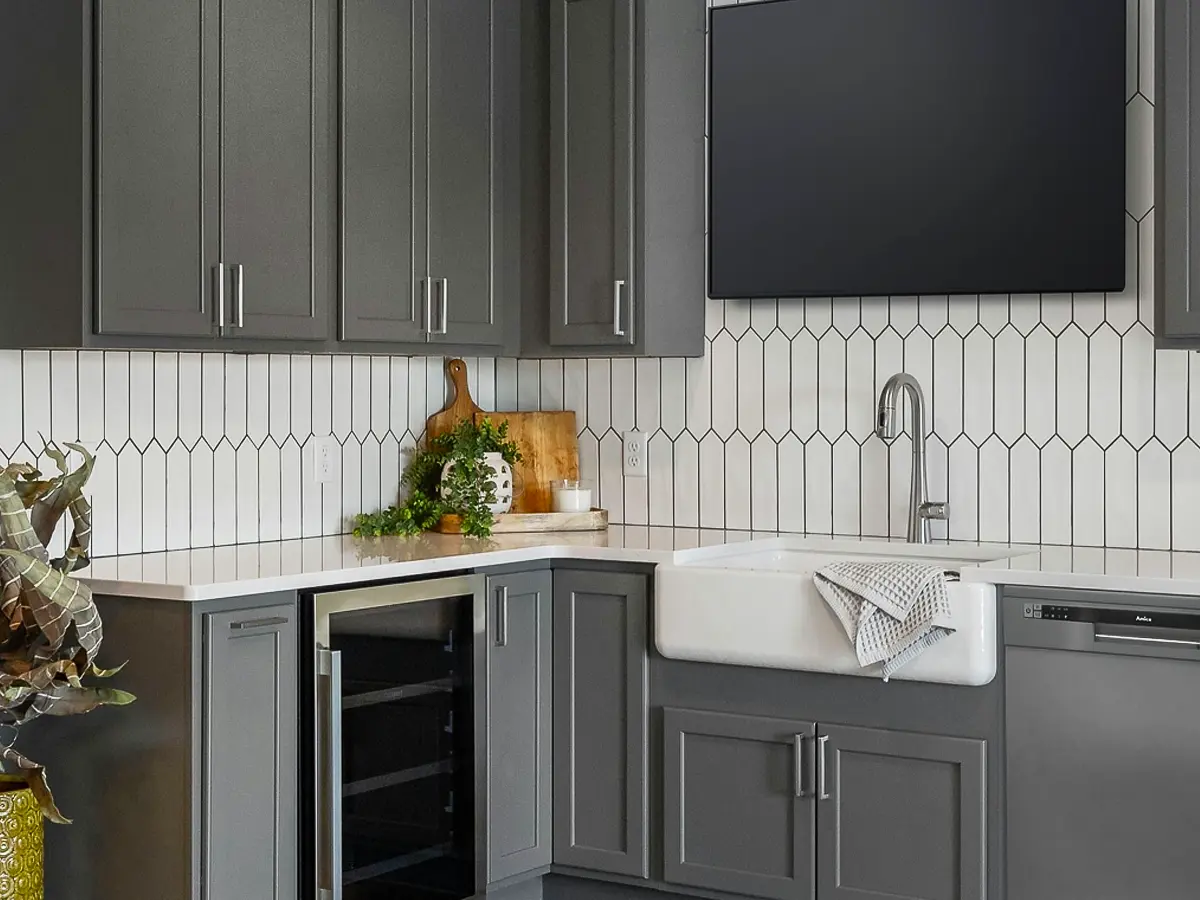 Contemporary gray kitchen cabinets with a farmhouse sink, geometric backsplash, and built-in wine cooler.