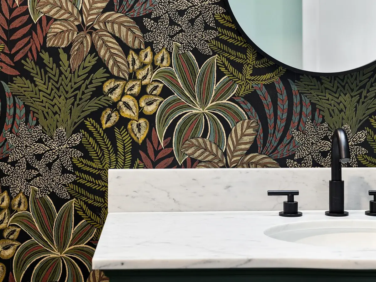 Bold bathroom design with floral wallpaper, a round mirror, and a white marble countertop with black fixtures.